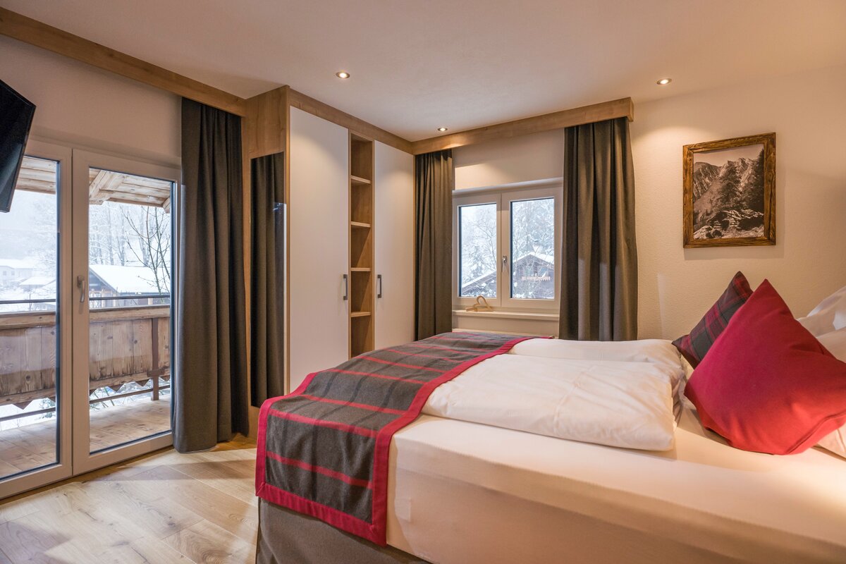 Schlafzimmer mit Bett und Balkon, der auf schneebedeckte Berge blickt – ideal für entspannende Nächte in der Natur.