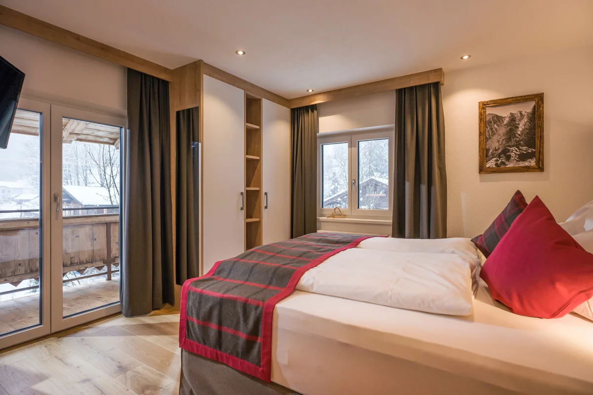 Schlafzimmer mit Bett und Balkon, der auf schneebedeckte Berge blickt – ideal für entspannende Nächte in der Natur.